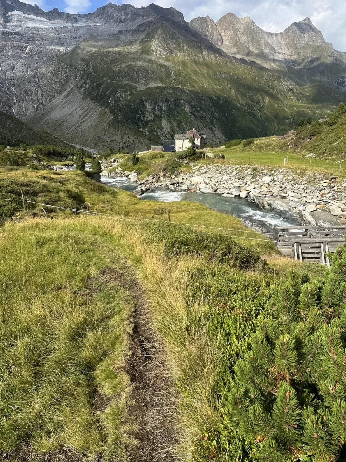 Berghütte am Fluss vor hohen Gipfeln